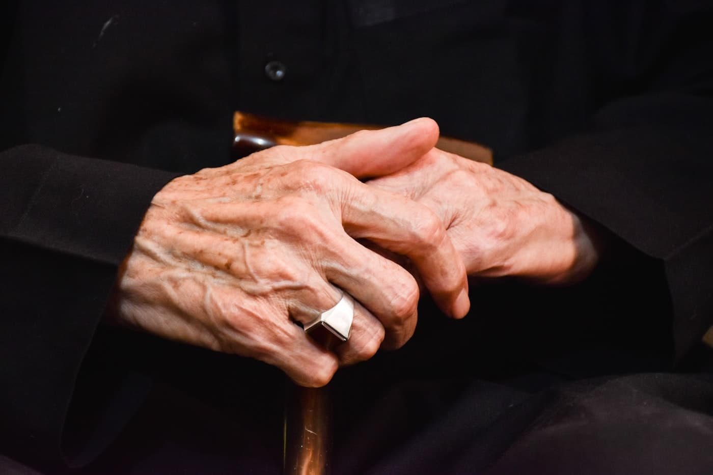 Sepia close-up of two pairs of hands intertwined on a checkered tablecloth in an American kitchen, warm light, suggesting love and generational connection