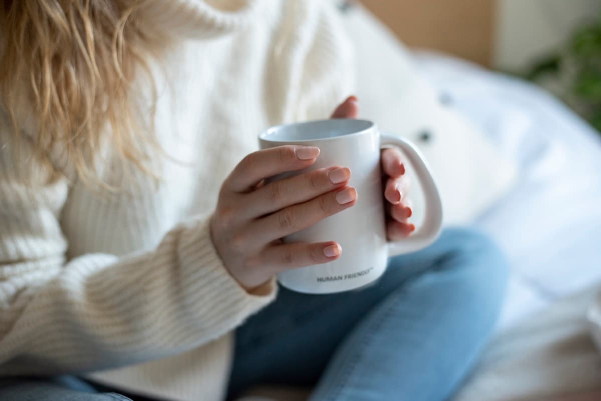 Woman with elegant hands cradling a warm coffee mug, soft natural light, quiet and intimate moment