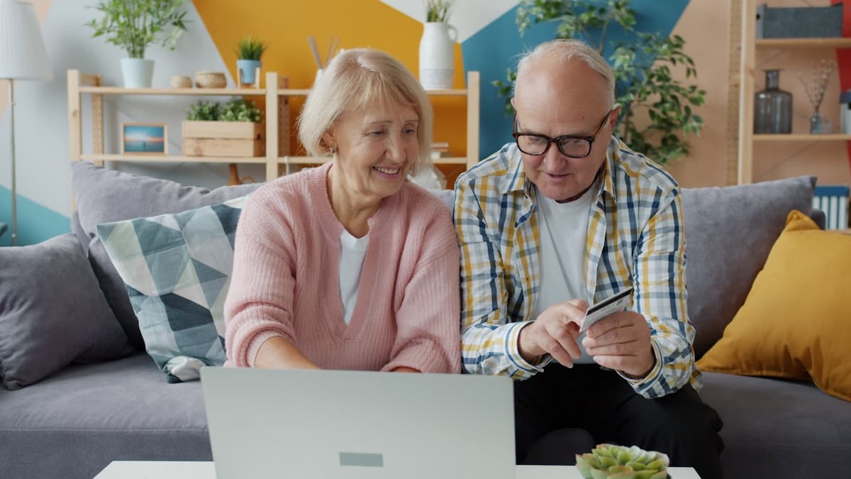 Elderly couple using laptop and credit card at home, cheerful and engaged