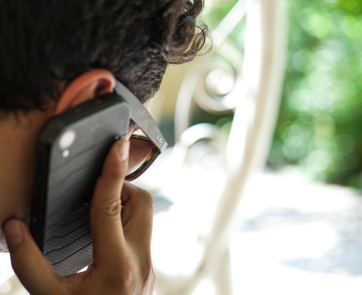 Person using smartphone while sitting near a white chair, relaxed and thoughtful