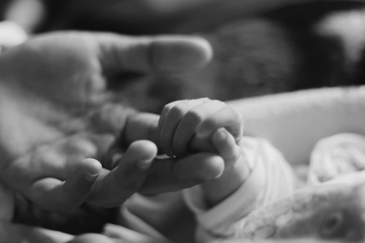 Black and white photo of a person gently holding a baby's hand — evoking Dorothy's years as a NICU nurse